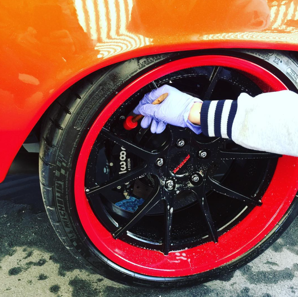 orange car with red tire and man cleaning rims